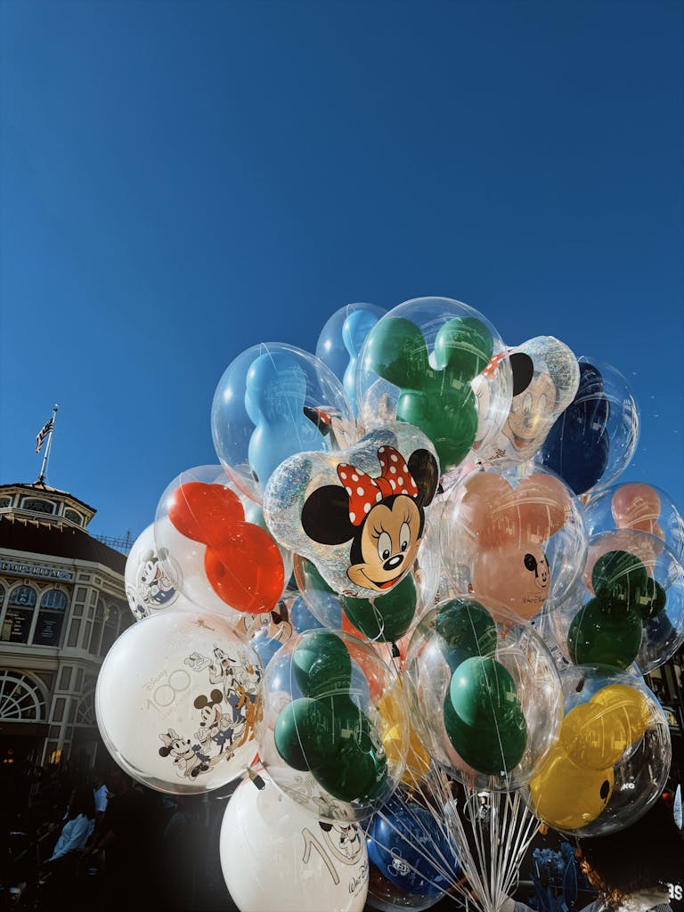 A cluster of vibrant Disney-themed balloons under a clear blue sky.